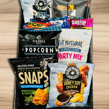 Assorted snack packages including popcorn, honey soy chicken, and party mix on a wooden surface.