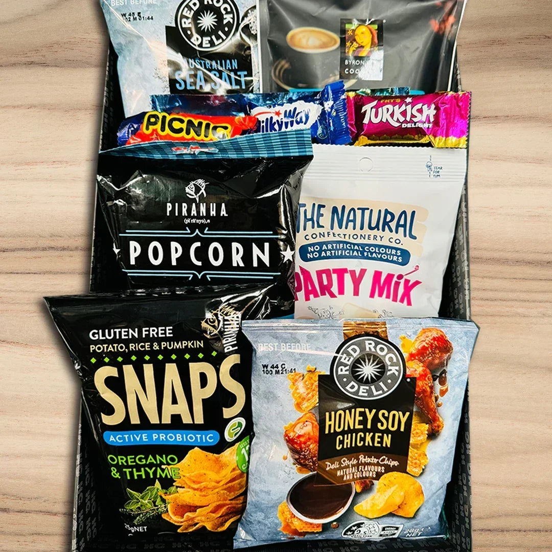 Assorted snack packages including popcorn, honey soy chicken, and party mix on a wooden surface.