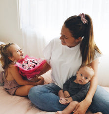 Woman sitting on a bed with two children, holding a baby and a toddler.
