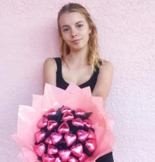 Woman holding a bouquet of pink heart-shaped balloons against a light pink background
