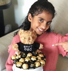 Child holding a teddy bear and a tray of chocolates, with a focus on the chocolates.