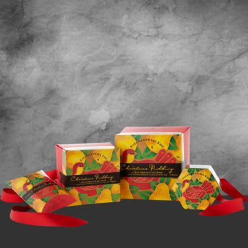 Pack of four colorful Christmas pudding boxes with bird and pear design, red ribbon on gray background