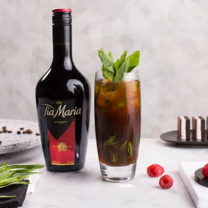 Tia Maria bottle with a cocktail garnished with mint and raspberries on a light background