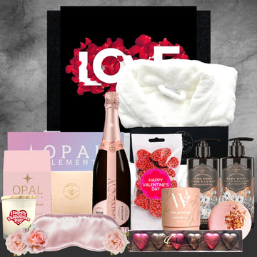 Valentine's Day gift basket with champagne, bath items, and other treats on a gray background.