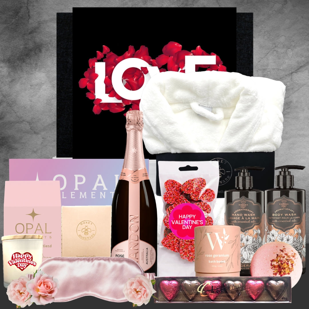 Valentine's Day gift basket with champagne, bath items, and other treats on a gray background.