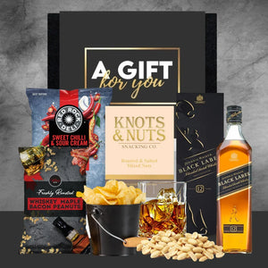 Gift set with snacks and a bottle of Johnnie Walker Black Label whisky on a gray background.