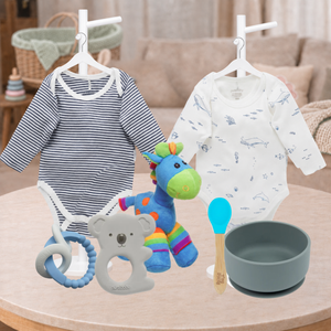 Two baby bodysuits hang on white hangers above a baby gear set on a wooden table. The left bodysuit is navy and white striped, and the right bodysuit is white with blue sea life prints.