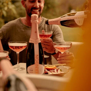 Person pouring champagne into a glass with another person holding a glass, outdoor setting.