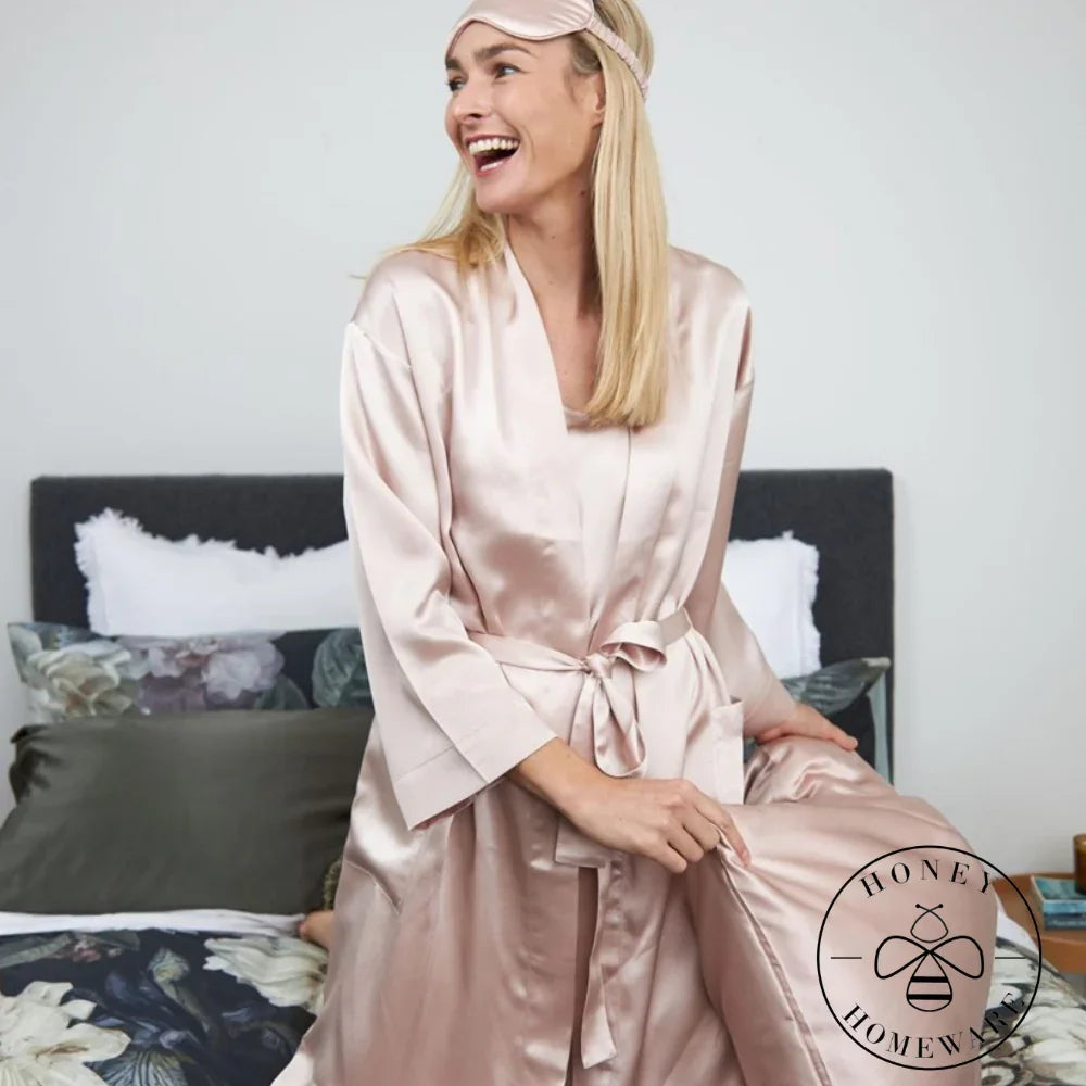 Woman in a pink satin robe sitting on a bed with a 'Honey & Home' logo.