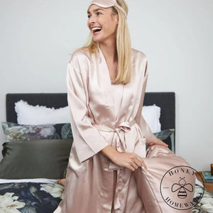 Woman in a pink satin robe sitting on a bed with a 'Honey & Home' logo.