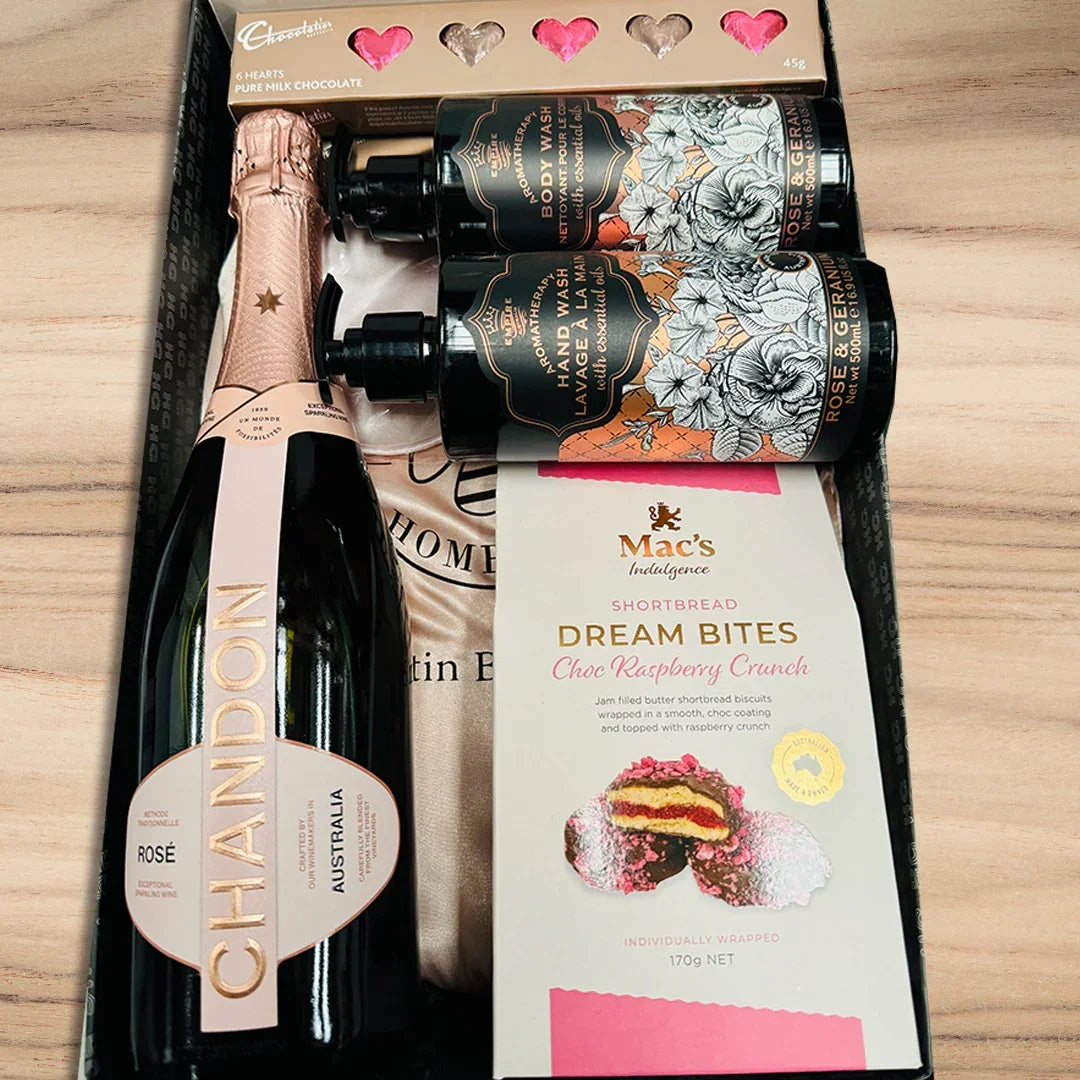Gift set with Chandon rose wine, Mac's shortbread, and chocolate bars on a wooden surface.