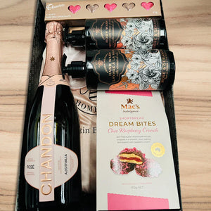 Gift set with Chandon rose wine, Mac's shortbread, and chocolate bars on a wooden surface.