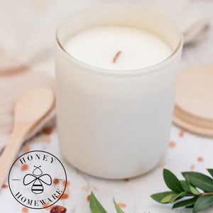 White candle in a glass jar with a wooden lid on a decorative surface, featuring the Honey Homeware logo.