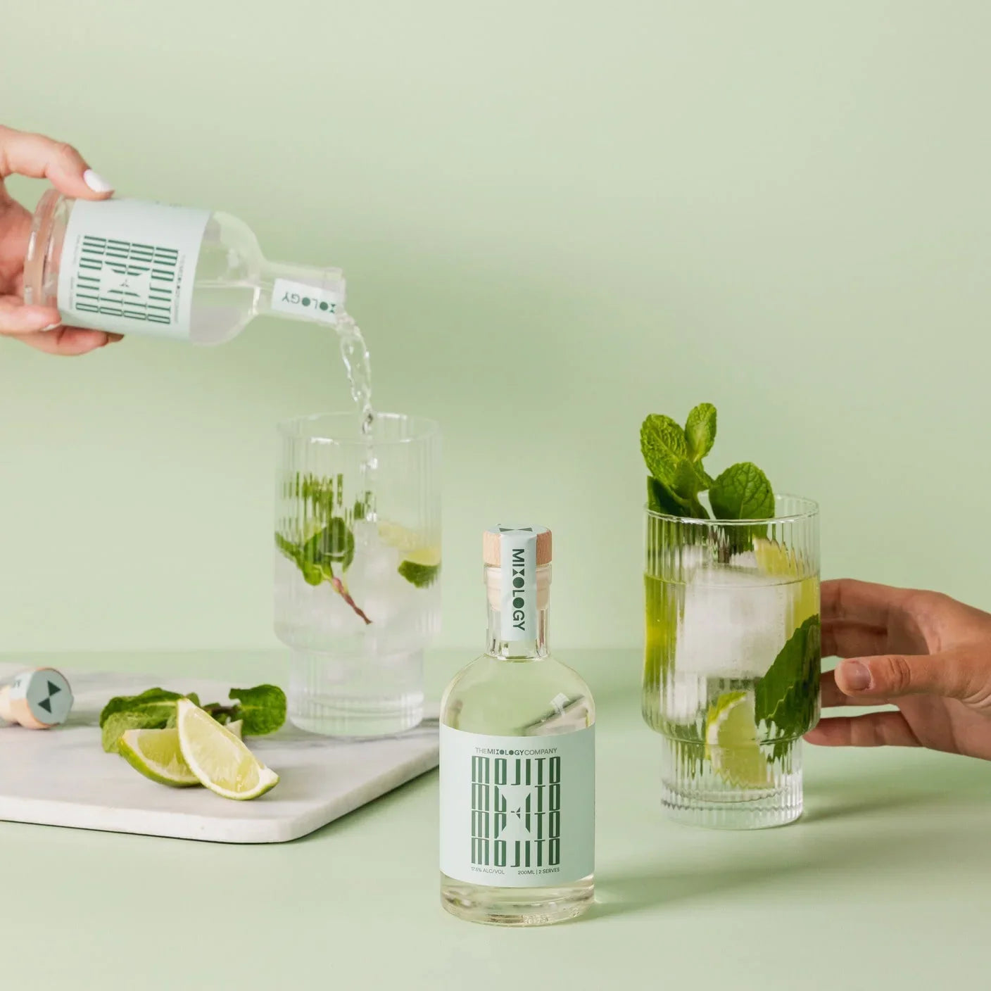 Person pouring a clear bottle into a glass with ice and lime on a light green background