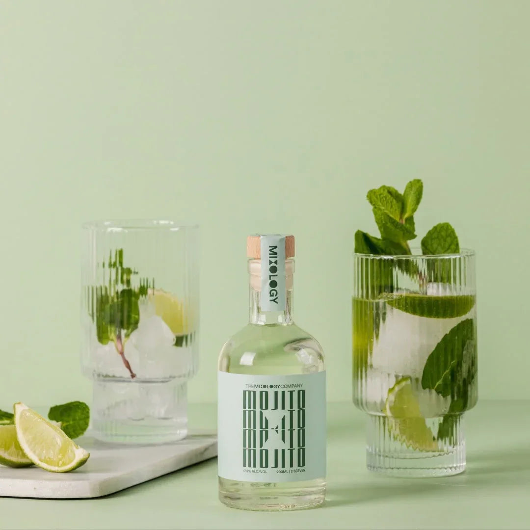 Bottle of gin with two glasses of gin and tonic on a light green background