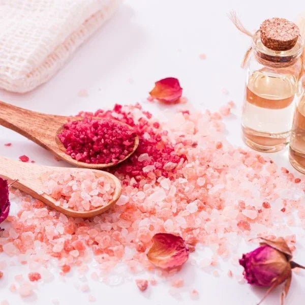 Pink bath salts with wooden spoons and rose petals on a white surface