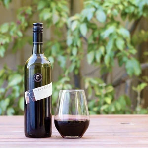 Bottle of wine and a glass on a wooden table with a blurred green outdoor background