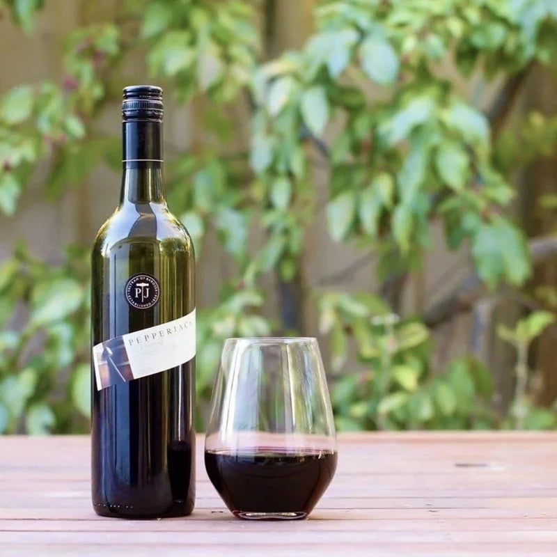 Bottle of wine and a glass on a wooden table with a blurred green outdoor background