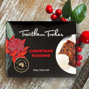 Trentham Tucker Christmas pudding packaging with a decorative flower and red berries on a wooden surface.