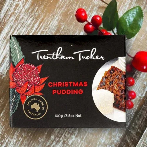 Trentham Tucker Christmas pudding packaging with a decorative flower and red berries on a wooden surface.