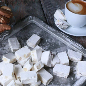 White nougat pieces on a metal tray with a cup of coffee in the background.