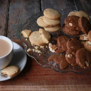 Assorted cookies on a decorative plate with a cup of tea on a wooden surface