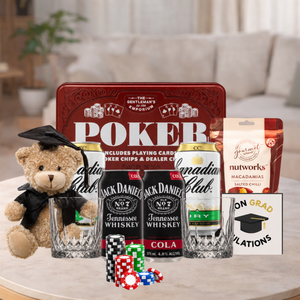 A graduation-themed poker gift set arranged on a light marble table in a softly blurred indoor setting. The set includes a red metal poker tin, two Jack Daniel's No.
