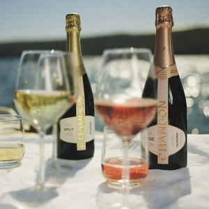 Two bottles of Chandon champagne with glasses on a table by a body of water.