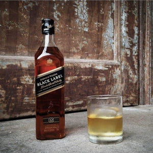 Johnnie Walker Black Label whisky bottle with a glass of whisky on a rustic wooden background